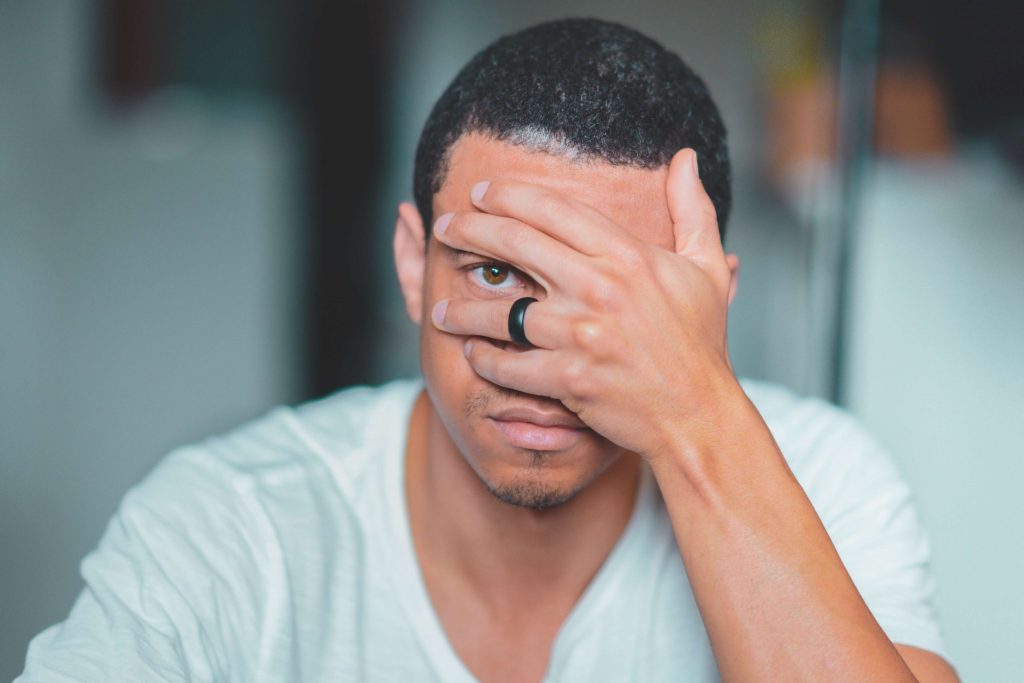 Mann sieht durch Finger und trägt schwarzen Ring